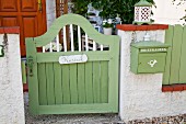 Green-painted wooden garden gate with name plate next to matching letterbox mounted on wall