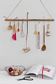 Kitchen utensils hung on suspended wooden rod with hooks above open cookery book, scissors and wire basket