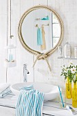 Round bathroom mirror with decorative rope frame in a white bathroom with wood-panelled walls