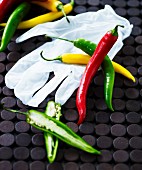 Various different coloured chilli peppers with a rubber glove