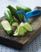Courgettes, partially sliced, with a peeler on a chopping board