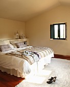 Double bed with fur blanket and white bed linen in minimalist attic bedroom