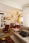 Pale couch and low table in front of brown armchair and dining area below window