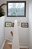 View down stairwell with view through window above framed photos on shelf