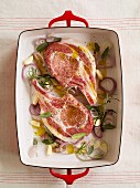 Raw pork chops with olive oil, herbs, onions and garlic in a roasting tin