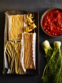 Dried pasta on a baking tray with tomato sauce and fresh fennel
