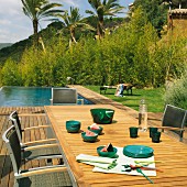 Blick von Holzdeck mit Outdoor-Essplatz auf angrenzenden Pool; Vegetation mit Palmen im Hintergrund