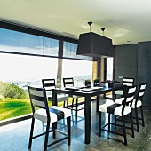 Black and white designer dining area next to continuous glass wall with view of landscape