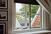 Sprossenfenster mit Messingbeschlägen im Giebel eines Dachzimmers; Blick auf Dachlandschaft und Bäume