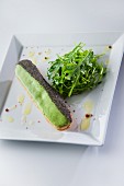 An éclair with salmon cream, wasabi glaze and poppy seeds served with rocket