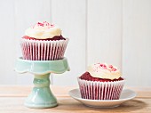Two Red Velvet cupcakes with white frosting on a plate and on a cake stand