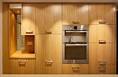 Küchenschrank mit Holzfront und Edelstahl Möbelgriffen, Kücheneinbaugeräte, seitlich integrierte Öffnung mit Blick auf Treppe