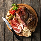 Tyrolean bacon on a board Schüttelbrot (crispy unleavened bread from South Tyrol) with conichons, lamb's lettuce and a knife