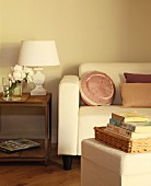 Stacked books on stool opposite sofa with elegant scatter cushions next to vintage-style table lamp with white lampshade on wooden side table