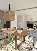 Pendant lamp with wicker lampshade above dining set with vintage chairs and patterned rug in front of lounge area in modern interior