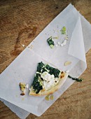 Slice of spinach pizza on a piece of paper on a wooden table