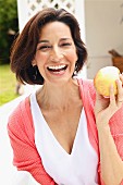 Dark-haired woman wearing top and cardigan holding apple