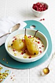 Poached pears in a creamy sauce with pomegranate seeds and pistachio nuts
