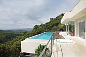 Weitblick in bewaldete Landschaft vom umlaufenden Balkon und Infinity-Pool eines modernen Ferienhauses