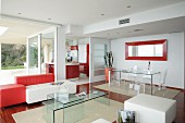 Open-plan interior with plexiglas and leather designer furniture, red accents and sliding door leading to kitchen in background