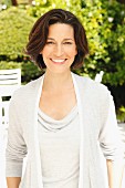 A brunette woman in a garden wearing a light grey top and a cardigan