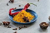 Turmeric powder, a dried chilli pepper, shiitake mushrooms and star anise on a plate and next to it