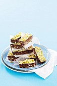 Stacked chocolate pistachio bars with coconut and biscuits on a plate
