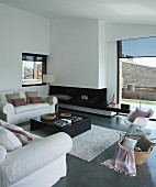 weiße Sitzgruppe vor Kamin in modernem Wohnraum; Klassiker Schaukelstuhl im Vordergrund