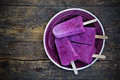 Four yoghurt and blueberry ice lollies on a wooden table (seen from above)