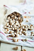 Roasted, salted pistachios falling out of a cup onto a tea towel