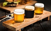 Drei Biersorten in einer Holzhalterung; helles Bier, dunkles Bier und India Pale Ale