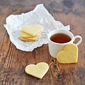 Kekse in Herzform mit Tasse Tee auf altem Holztisch