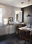 Retro pendant lamp above dining table made from glass table top on wooden trestles in simple kitchen with black accent wall