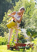 Lachendes Mädchen beim Giessen von Topfpflanzen im Garten