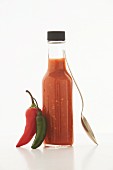 A bottle of chili sauce, fresh chilli peppers and a spoon
