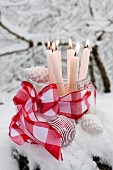 Brennende Kerzen in einer alten Glasschütte mit roter Schleife und weißem Christbaumschmuck, im Schnee