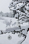 Two wooden deer figurines and white Christmas baubles on snow-covered branch