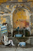 Wash area in shabby-chic interior, vintage zinc bowl on stone bench below water spouts in arched niche; Mediterranean, French style