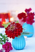Zinnia and snap dragons in turquoise glass vases with lit candles in background