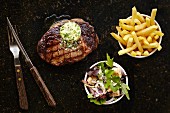 Grilled steak with garlic and herb butter served with chips and a salad