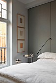 Bed with white bed linen against floor-to-ceiling panels covered in grey fabric in traditional, elegant interior