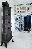 Antiker, kunsthandwerklicher Kaminofen und nostalgisches Wandboard mit Kleiderhaken auf blauer Blumentapete