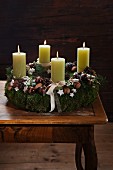Rustic Advent wreath with four lit green candles decorated with walnuts, moss and pine cones