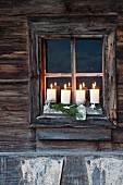 Rustic Advent arrangement with four lit candles on windowsill of weathered wooden house