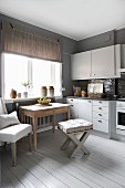 Dining area below window with rustic wooden table and stool in pale grey fitted kitchen