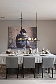 Festively set dining table below candle chandelier and modern artwork on wall