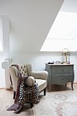 Antique armchair next to wooden chest of drawers in bright attic room