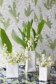 Lily of the valley in designer vases in front of wallpaper with lily of the valley pattern