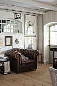 Brown leather armchair below collection of artworks on wall in rustic interior
