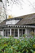 Blick vom Garten auf Wohnhaus mit Anbau, an Fenster und Traufkante befestigtes Zierbrett grau lackiert